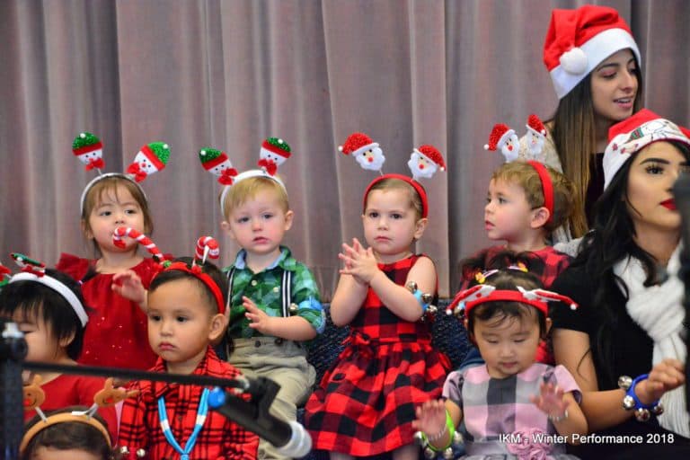Children in Christmas attire perform on stage.