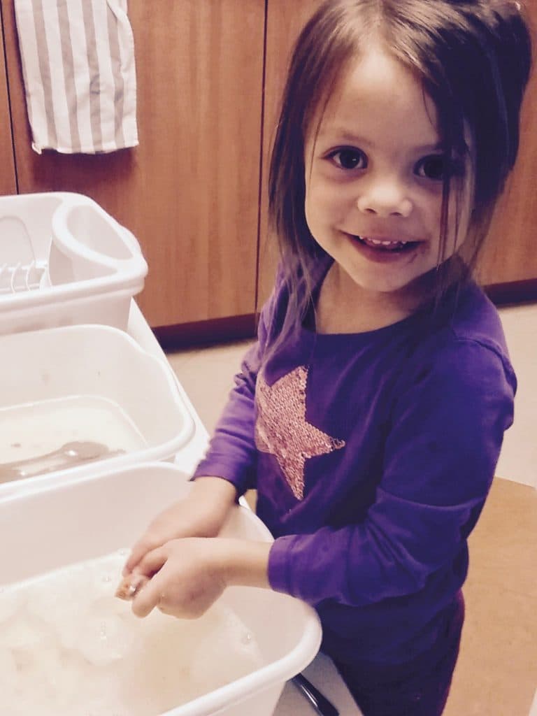 Smiling girl washes hands in a sink.