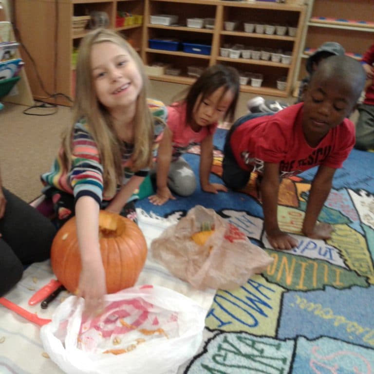Three children carving pumpkins on a rug.