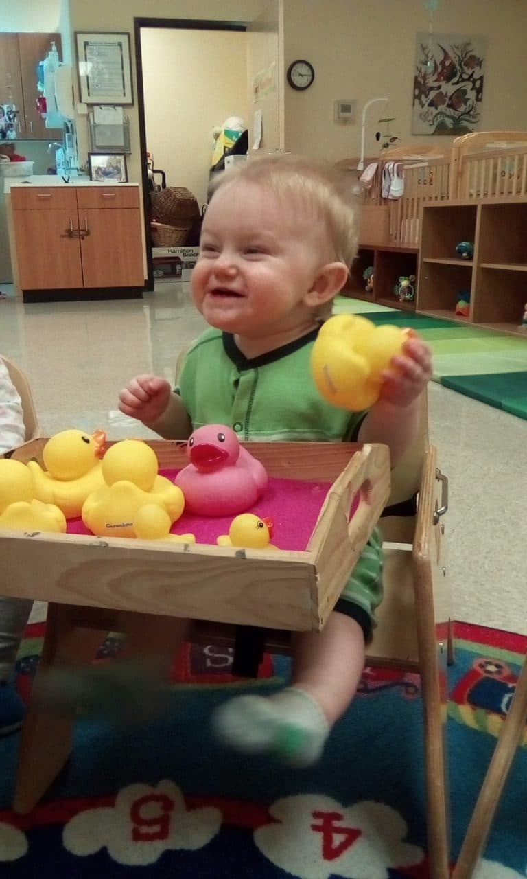 Toddler playing with rubber ducks in a high chair.