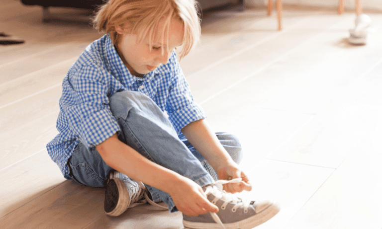 Child tying shoelaces on wooden floor.