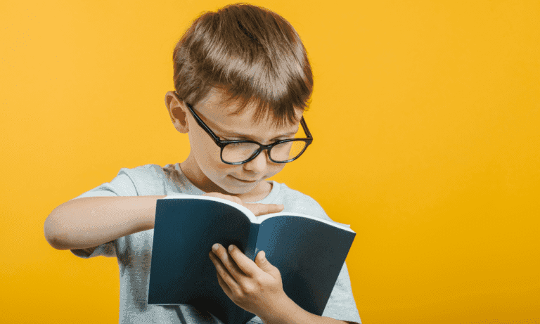 Boy wearing glasses reads a book.