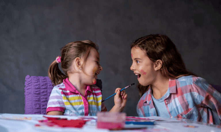 Two girls playfully paint each other's faces.